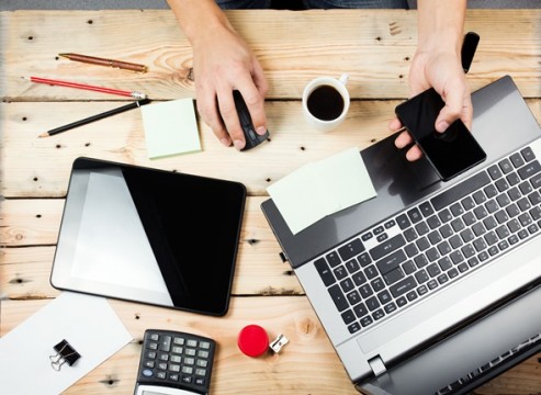 Man at wooden table with laptop and smartphone
